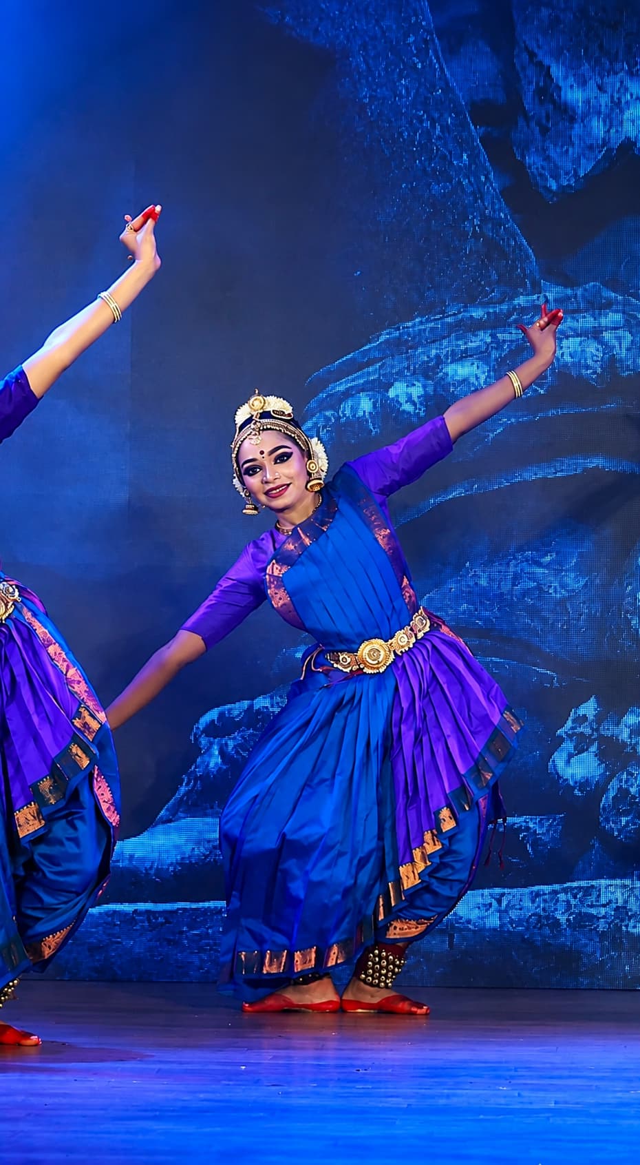 Dancers performing Bharatanatyam in traditional blue and gold costumes on stage